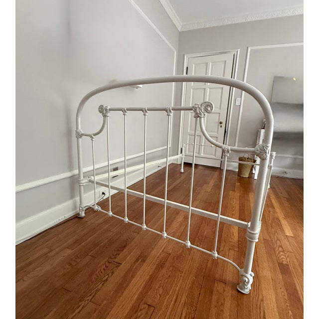 Beautiful antique white full-size bed frame featuring ornate detailing, conical plugs, and a sturdy heavy iron...