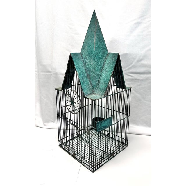 A tall vintage architectural birdcage featuring a dramatic peaked roof with a weathered green finish and slender black...