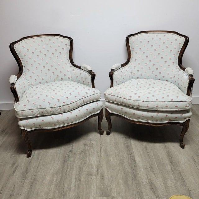 A handsome pair of French Louis XV–style bergère armchairs, featuring sculpted walnut frames with softly carved cabriole...