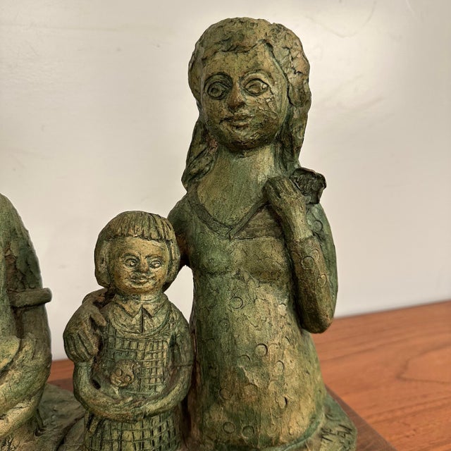 The sculpture is made of clay with a green, aged patina finish. It depicts a father holding a baby, a mother, and a young...