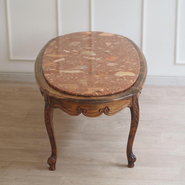 This charming vintage coffee table boasts a bold, oval marble top in a warm terracotta shade with beige and light...