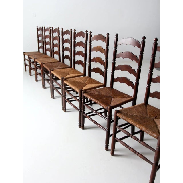 A set of eight antique ladder back chairs, defined by their tall, slender silhouettes and timeless rustic appeal. Each...