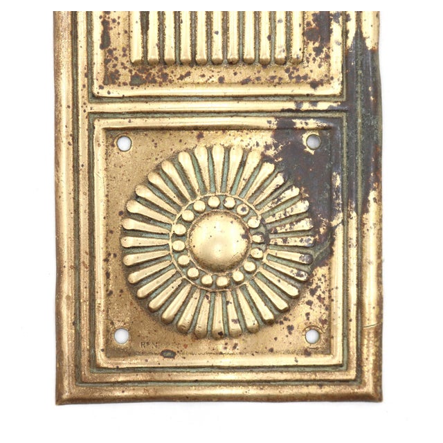 Aesthetic pressed brass door push plate featuring top and bottom sunburst rosettes separated by a central reeded column....
