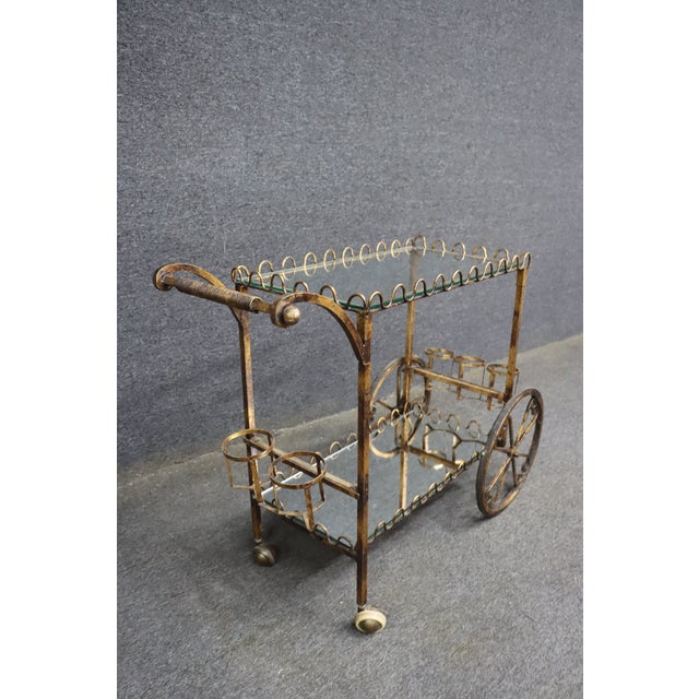 Stylish Hollywood Regency bar cart crafted from iron and metal with a gold-tone finish. Features two open shelves with...
