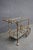 Stylish Hollywood Regency bar cart crafted from iron and metal with a gold-tone finish. Features two open shelves with...