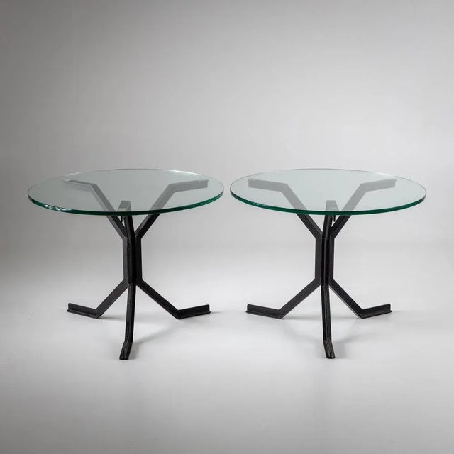 Pair of side tables with round glass tops and three-legged iron frames made of black lacquered T-beams.