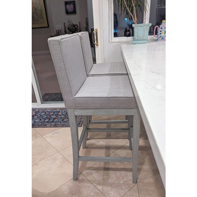Two gray bar stools with sumptuous grey fabric seats and unique painted wood.There are no identifying manufacturers on the...