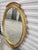 A distinctive carved wood oval form mirror by Carver's Guild in the Neoclassical style. The Newport mirror is painted in...