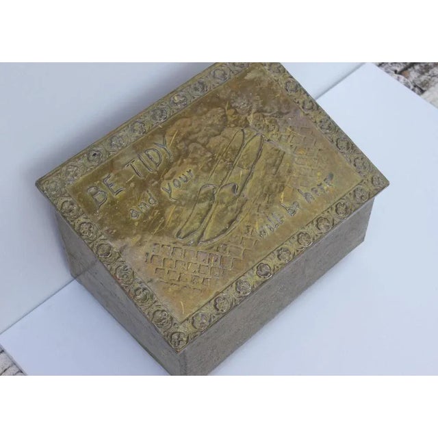 A brass box with a sloping lid, which is embossed: Be tide and your shoes will be here. There are forged relief ornaments....