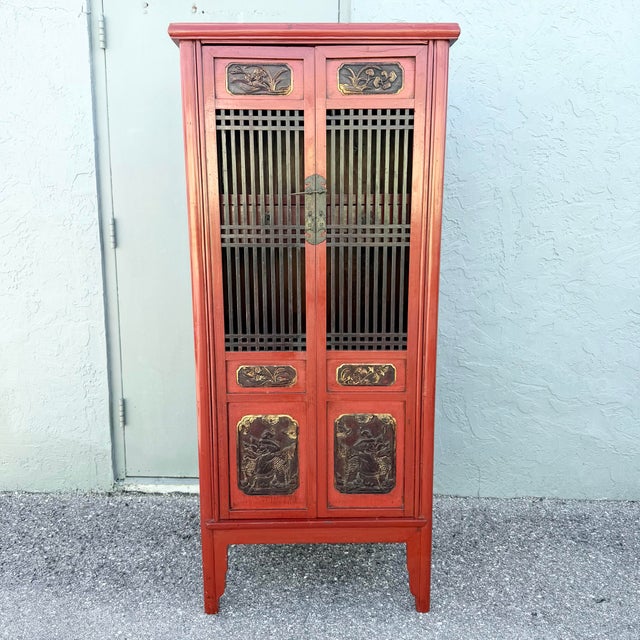 Striking vintage Chinese cabinet crafted in wood with a rich red painted finish, contrasting dark lattice doors, and...