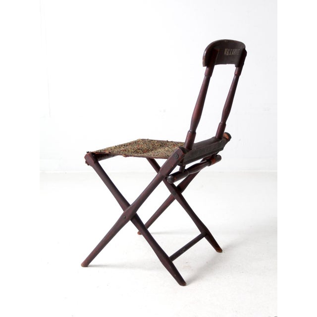 This antique folding camp chair, with a dark wooden frame and woven seat, is stenciled 'Weinert.' This name suggests...