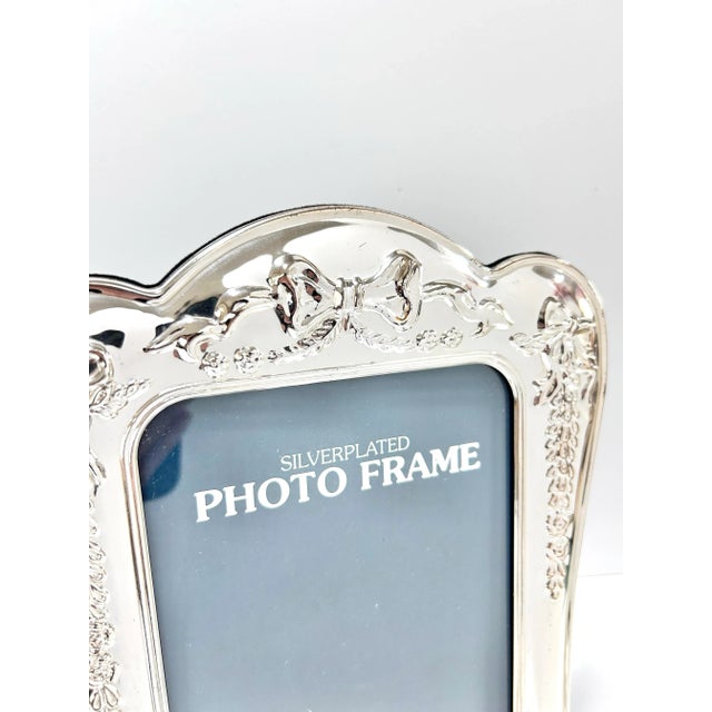 An elegant vintage silverplate picture frame featuring detailed repoussé decoration with bows, floral swags, and scrolling...