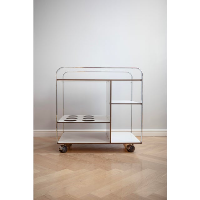 An architectural serving trolley from the 1980s with a chrome frame and white shelves. It has unusual compartments and a...