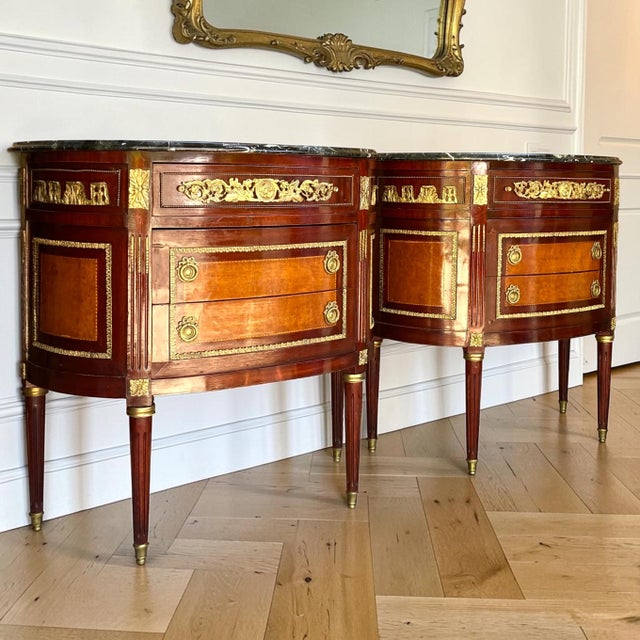 Exceptional pair of French Louis XVI style demilune commodes featuring richly figured mahogany veneers, dramatic marble...