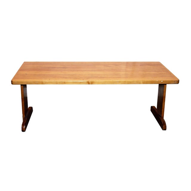 Medium tone wood coffee table. The smooth geometry of the trestle base points to mid 20th century Modern styling. The...