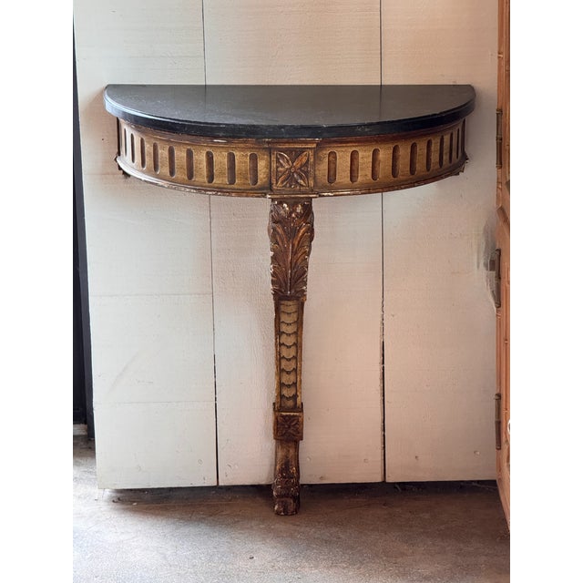 Giltwood wall mount console of demilune form with a black marble top above a frieze carved with vertical fluting, centered...