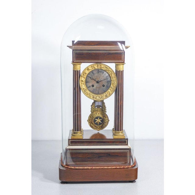 Pendulum clock with inlaid wooden portico structure and glass bell. period late 19th century materials inlaid wood....
