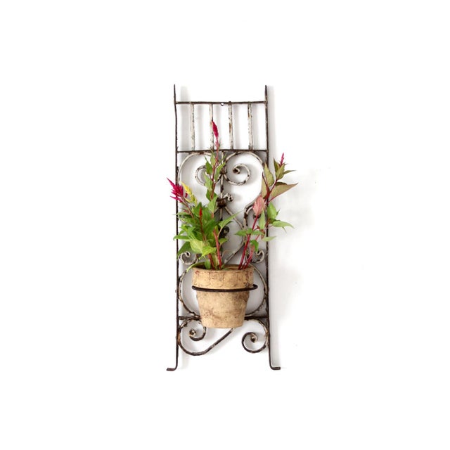 This vintage wrought iron wall planter features scrolling ironwork, a weathered white painted finish, and a small floral...