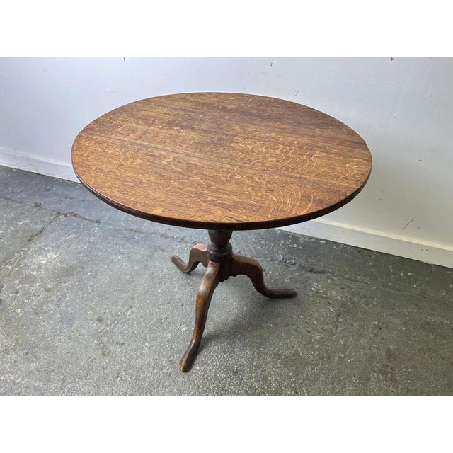 A 19th century Georgian-style oak tilt-top occasional table. The circular top, displaying a rich figured grain and...