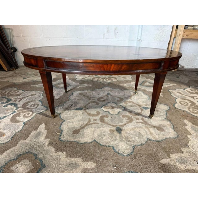 Vintage regency style Oval leather top flame mahogany coffee table on casters. by Weiman. It features an oval table top,...