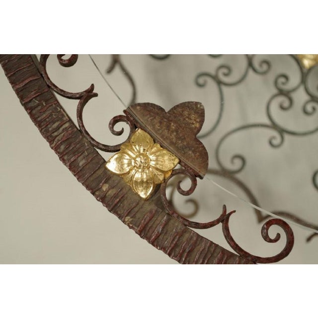 Openwork wrought iron coffee table with a transparent glass top, standing on three twisted feet linked by a stretcher made...