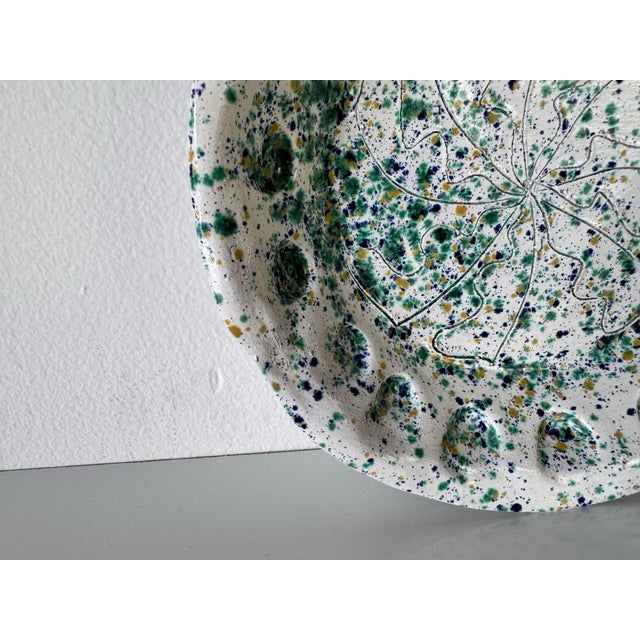 This vintage handmade pottery plate features a vibrant hand-painted design, with speckled splashes of green, blue, and...