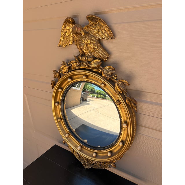 An antique Federal or Regency style giltwood convex mirror crowned with a carved eagle, its wings outstretched above a...
