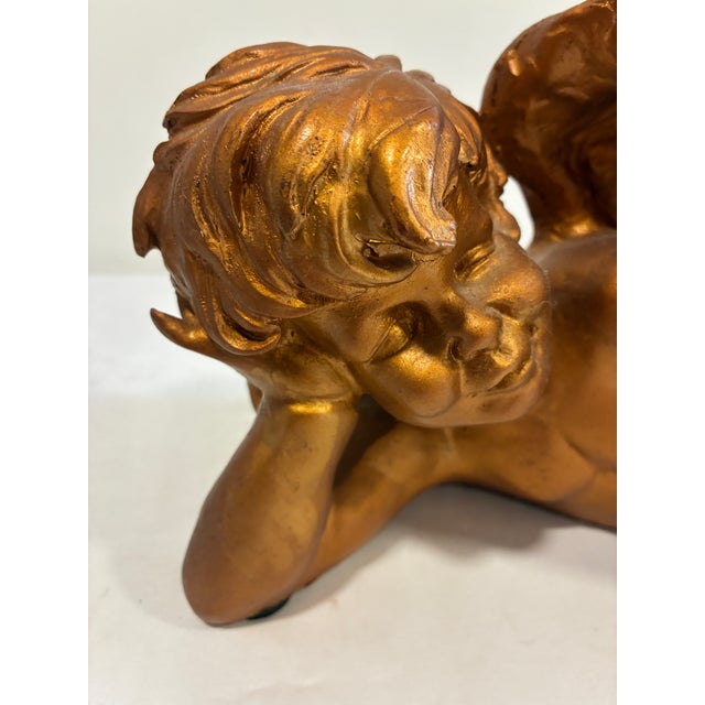 A beautifully reclining cherub finished in a rich antique gold tone. Likely crafted from plaster or chalkware, this...