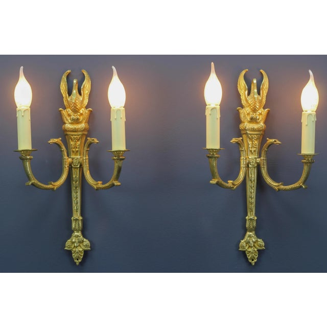 A pair of French Empire-style gilt bronze sconces. These beautiful wall lights are richly decorated with bronze details...