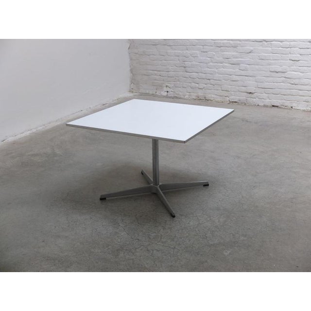 Early side or coffee table designed by Arne Jacobsen in 1968. This example features a square white laminated top with an...