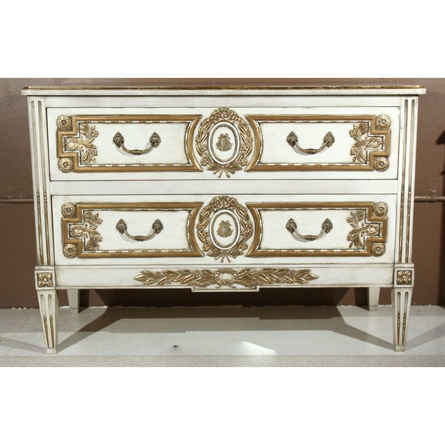 A very unique two-drawer commode, circa 1940's, thoroughly creme peinte and parcel gilded, the rectangular beveled top...