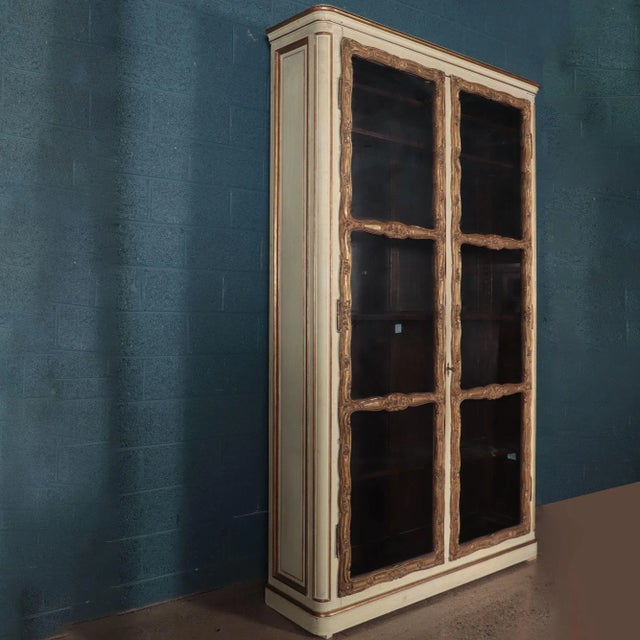 An imposing pair of cream painted and parcel gilt large bookcases, with two glass front doors each opening to five...