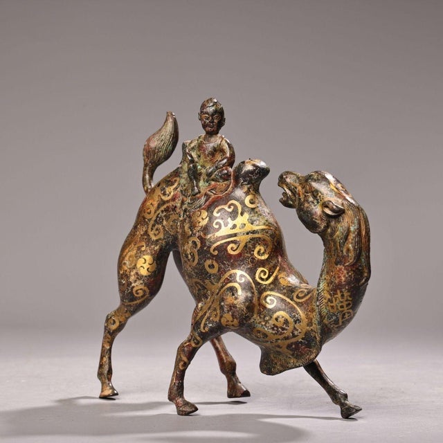 This is a finely detailed cast bronze figurine featuring a camel with a rider seated on its back. The piece is decorated...