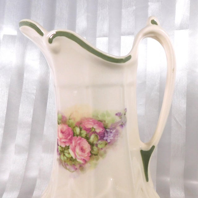 This is white shaped picture with a pink and purple floral design and green trim. It is by Sueramics from the San...