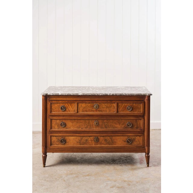 This elegant 19th-century French commode features a striking grey marble top and a three-drawer design adorned with...