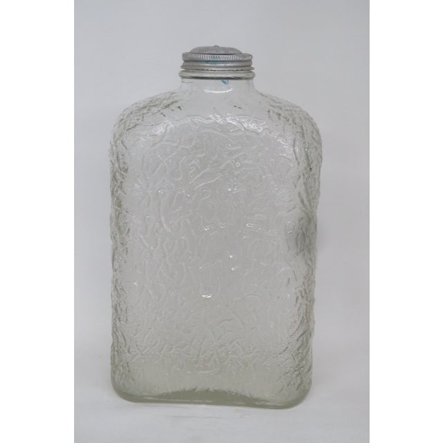 This gorgeous mid-century glass bottle features a lovely clear color and an embossed design that wraps around the entire...