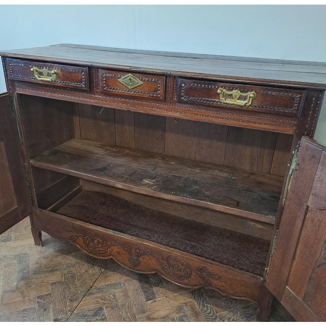 This elegant French carved oak buffet is a charming example of provincial craftsmanship. It features a beautifully aged...