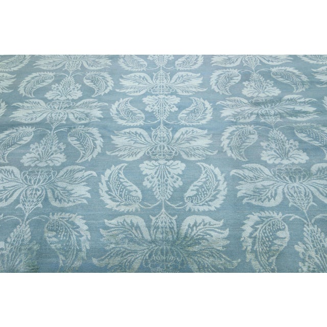 This contemporary Nepalese rug embraces a light blue floral motif that spans its all-over design. Its intricate details...