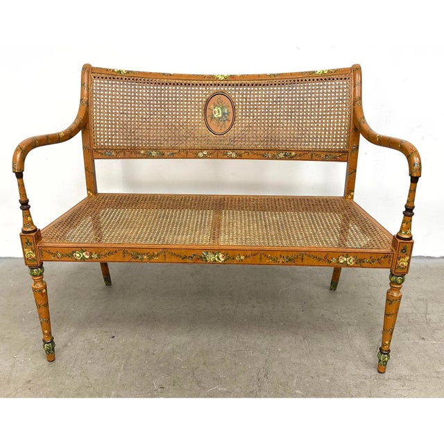 Elegant vintage Sheraton-style settee featuring a warm, honey-toned wood frame adorned with delicate painted floral details.