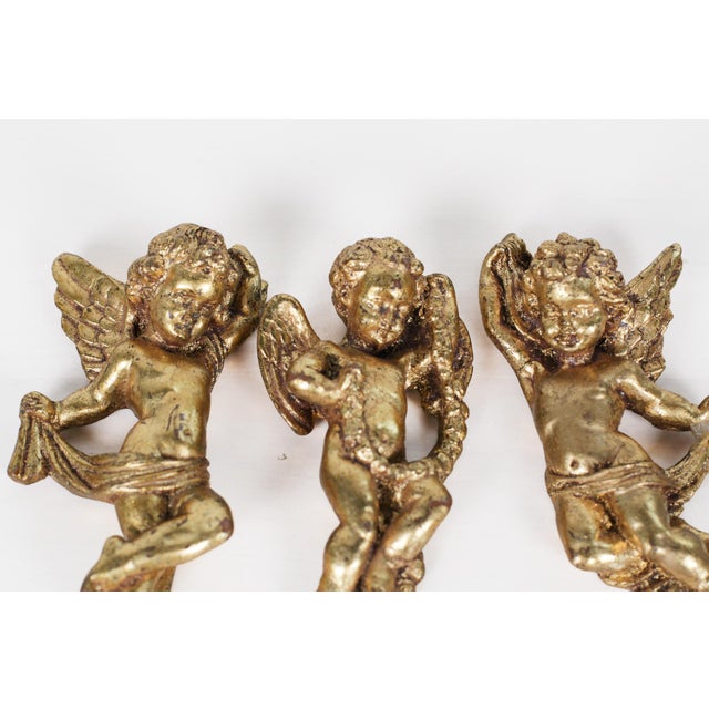 Gorgeous set of three mid-century French gold leaf gilded cherubs, each featuring detailed wings and flowing drapery, and...