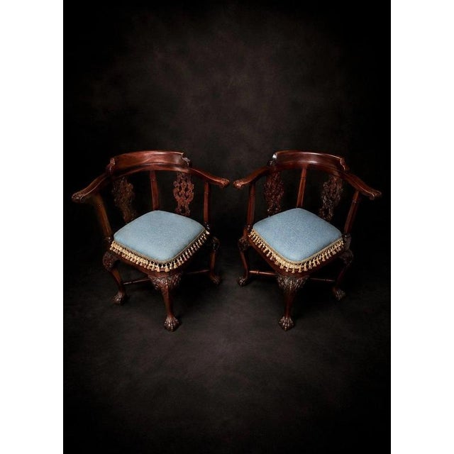 An elegant and highly decorative pair of carved mahogany corner chairs in the Chippendale style, combining graceful...