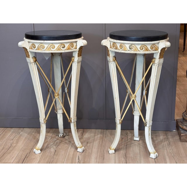 A pair of early 20th C. Northern European cream painted and parcel-gilt pedestals, each with a circular black marble top...