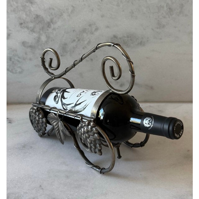 Vintage metal wine bottle holder with a swirl handle and grape and grape leaf addornments.