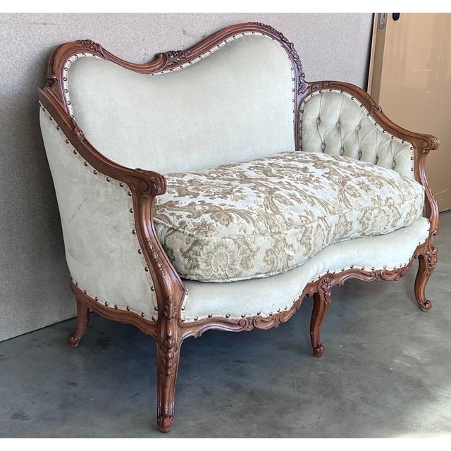 An antique Victorian sofa offers walnut frame in serpentine form having carved floral crest over button back upholstery,...