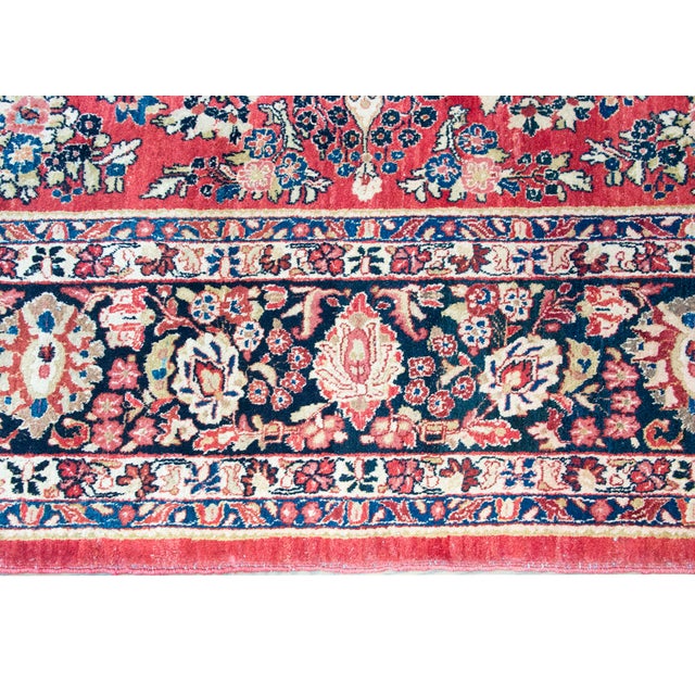 This hand-woven Persian Sarouk rug from the 1930s features a vibrant red field densely populated with intricate floral...