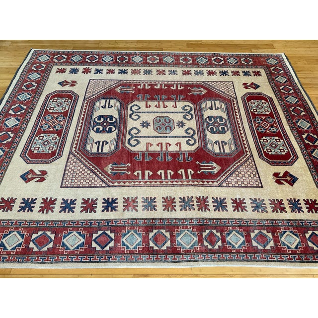 This hand-knotted wool rug features a bold Kazak design with tribal medallions, latch-hook symbols, and stepped borders....