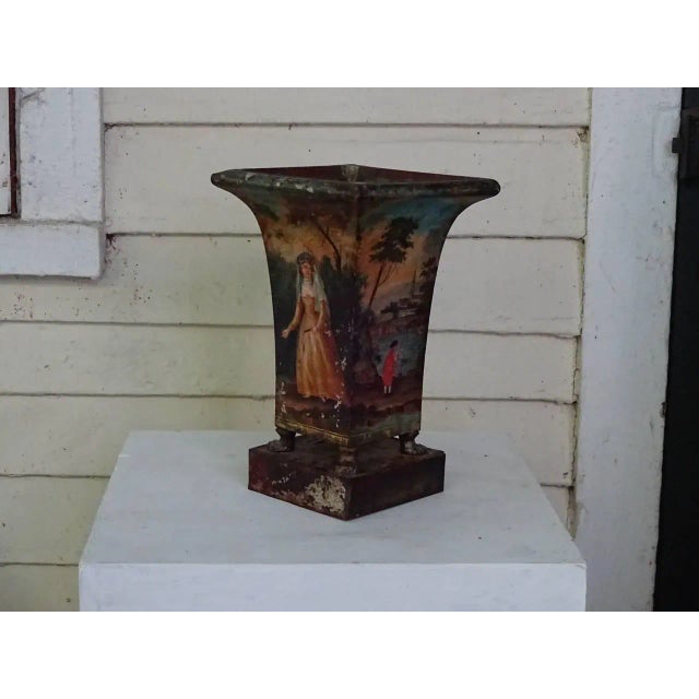 Pair of tole peinte beaker form jardinieres with pastoral figures and scenery on all four sides. Claw feet support each...