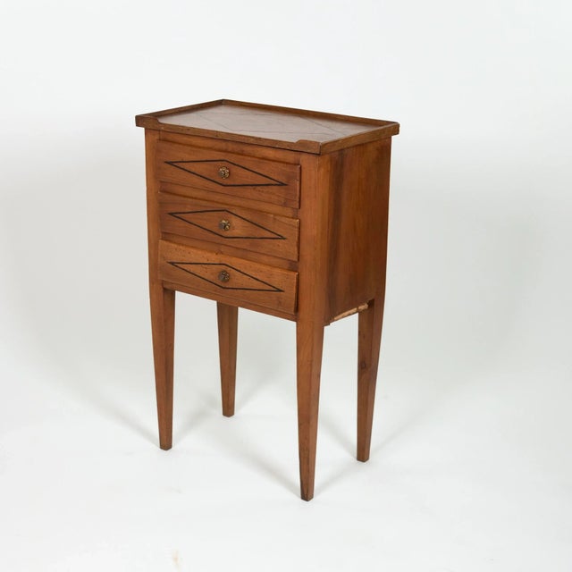A petite French walnut bedside chest of drawers, circa 1850, featuring three drawers with central pulls, each drawer...