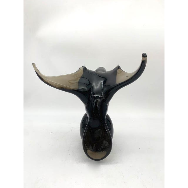 A decorative blown glass sculpture depicting a stylized bird, characterized by soft, clean lines. The body features a...