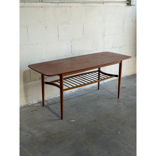 This rectangular teak coffee table combines a long narrow top with a full-length slatted lower shelf. Rounded corners and...